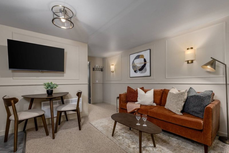Modern living room with brown leather sofa, wooden dining table, wall-mounted TV and designer lighting