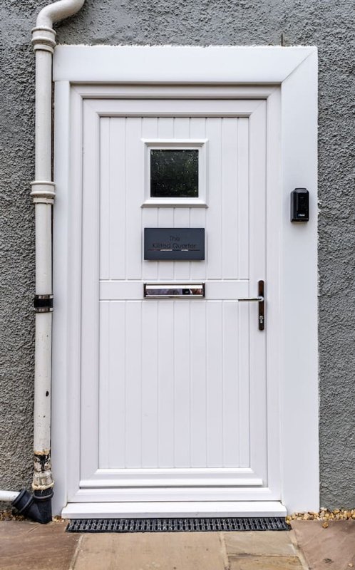 White front door with small windows, letterbox and handle on grey rendered wall