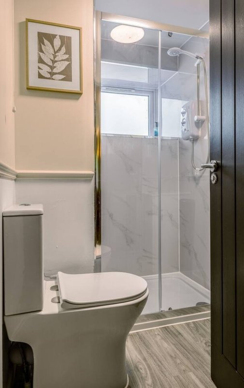 Modern bathroom with toilet, enclosed shower stall, marble tile, and botanical wall art