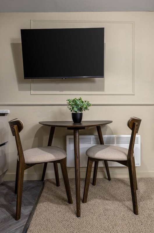 Modern living room with wall-mounted TV, wooden dining table, two chairs and potted plant