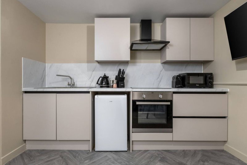 Modern kitchen with white cabinetry, marble backsplash, built-in oven and black range hood
