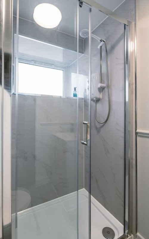 Modern bathroom with walk-in shower, glass enclosure, rainfall showerhead and circular ceiling light