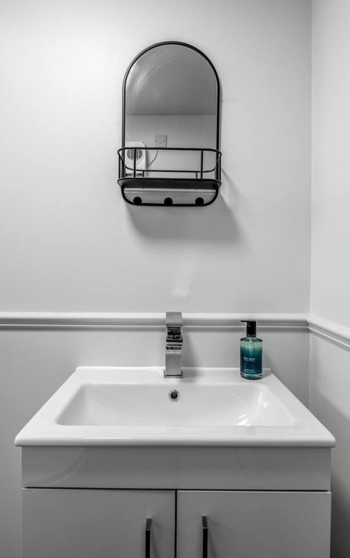 Modern bathroom sink with white countertop, chrome faucet, arched mirror and shelf