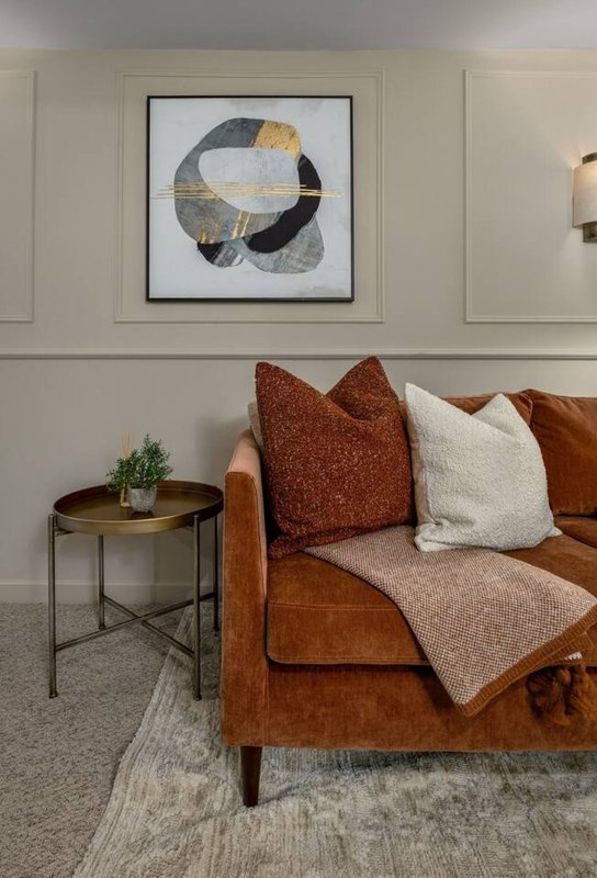 Living room with tan leather sofa, decorative pillows, side table, and abstract wall art