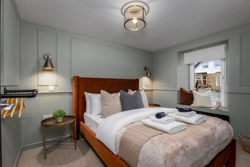 Bedroom with wooden bed frame, white bedding, pendant lights, and ensuite visible through doorway