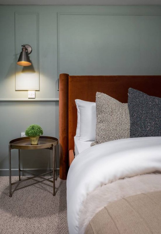 Modern bedroom with terracotta headboard, white bedding, patterned pillows and wall-mounted lamp