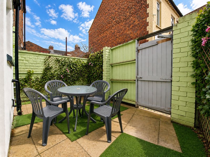 Small garden patio with green-painted brick walls, round table, four dark chairs, and ivy climbing