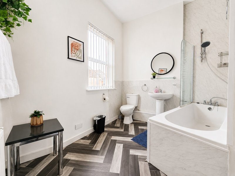 Modern bathroom with white bathtub, toilet, pedestal sink, chevron flooring and window