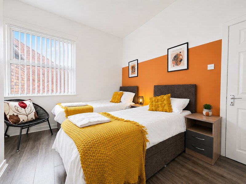 Bright bedroom with two beds, orange accent wall, yellow bedding, and large window