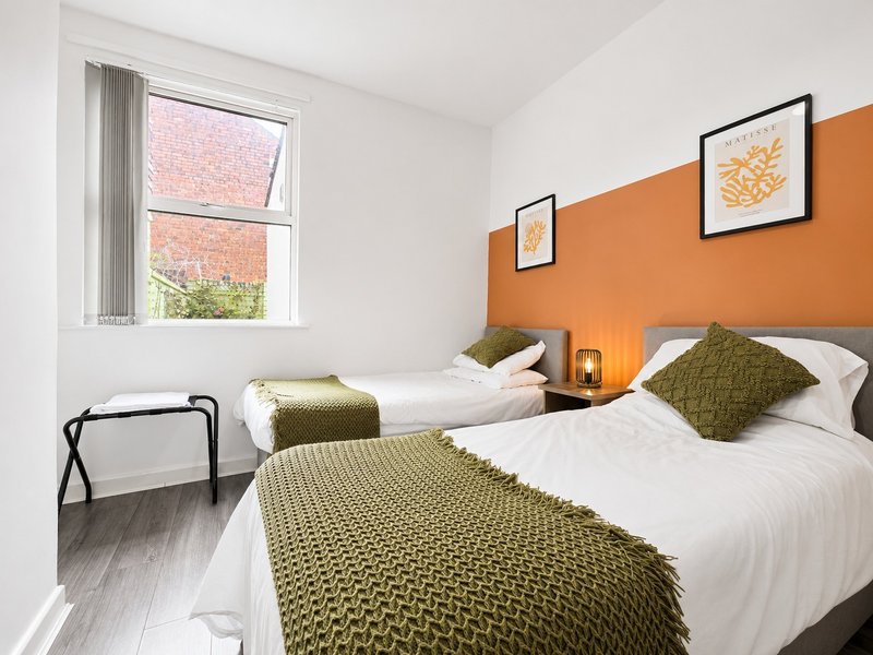 Modern twin bedroom with orange accent wall, white bedding, olive throws and framed botanical prints