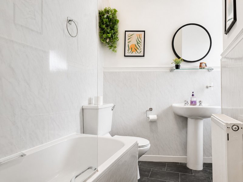 Clean modern bathroom with white subway tiles, bathtub, pedestal sink, and round mirror