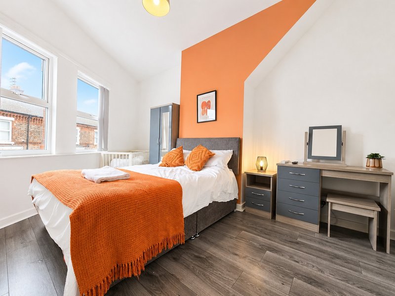Bright bedroom with orange accent wall, double bed, wooden floor, and large windows