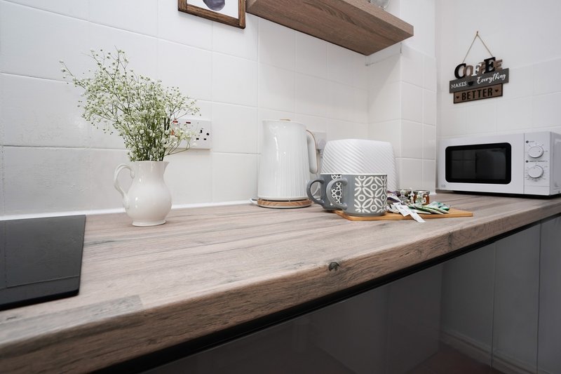 Modern kitchen counter with white kettle, microwave, flowers in pitcher and decorative items