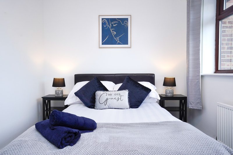 Modern bedroom with double bed, navy blue pillows, white bedding, and framed abstract wall art