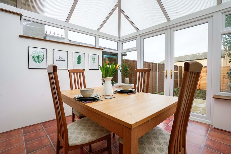 Bright conservatory with wooden dining table, four chairs, plant, wall art and garden view