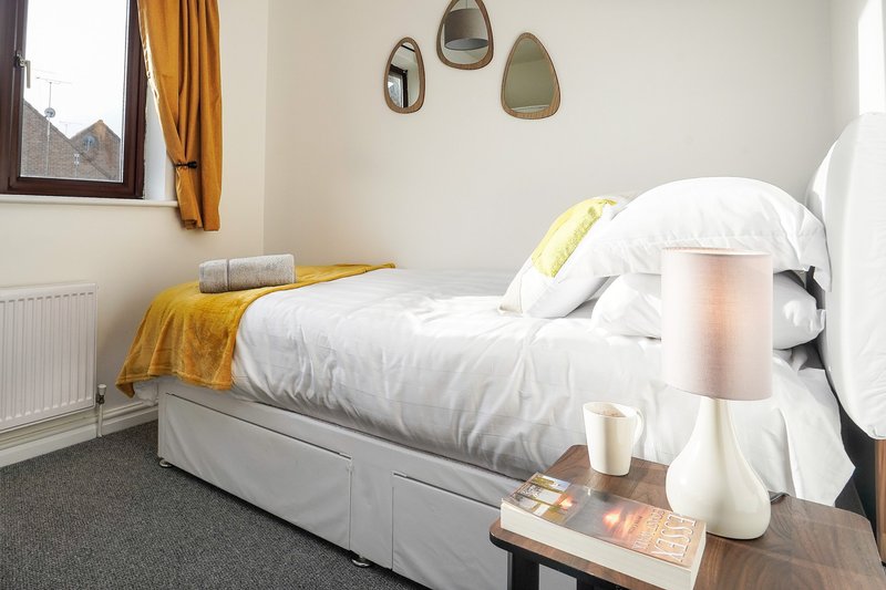 Modern bedroom with single bed, white bedding, yellow throw, and wall-mounted mirrors