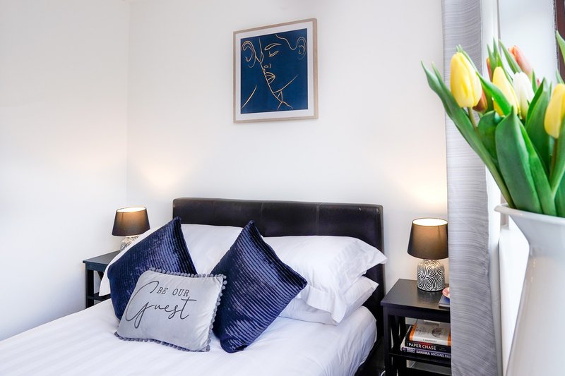 Bright bedroom with double bed, navy headboard, white bedding, yellow tulips, and wall art