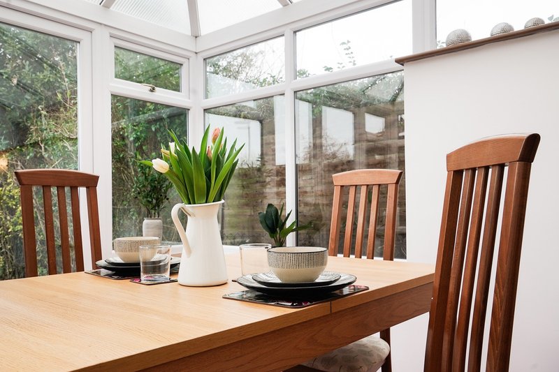 Bright dining room with wooden table, chairs, and plants near large windows