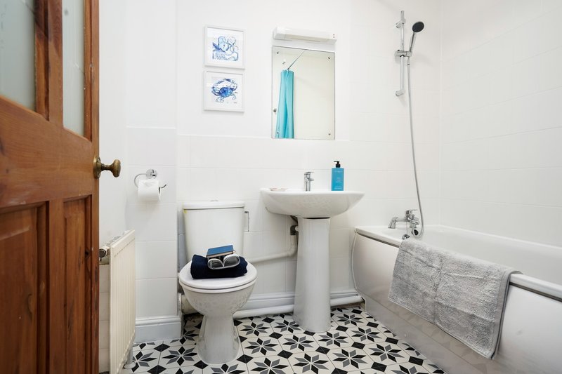 Bathroom with toilet, pedestal sink, bathtub, patterned floor tiles and wall art