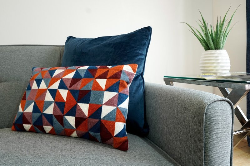 Grey sofa with blue and patterned cushions, side table with potted plant