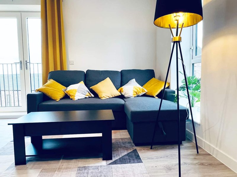Modern living room with dark blue corner sofa, yellow cushions, black coffee table and floor lamp