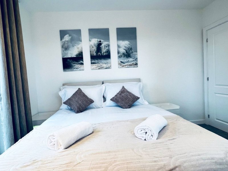 Bright bedroom with double bed, white bedding, decorative wave artwork above headboard