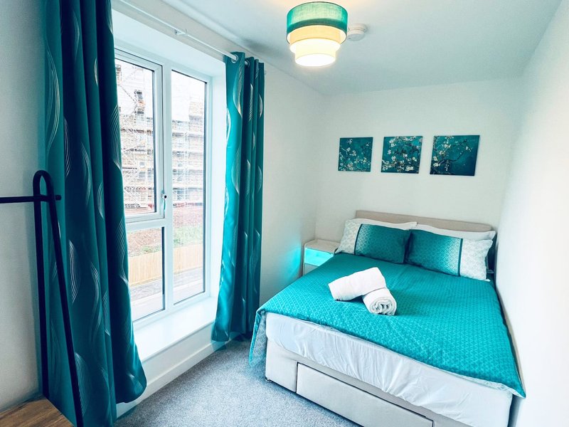 Bright bedroom with turquoise bedding, teal curtains, window with city view, ceiling light fixture