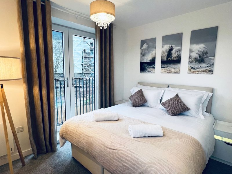 Bedroom with double bed, white bedding, decorative cushions, balcony doors and wall art