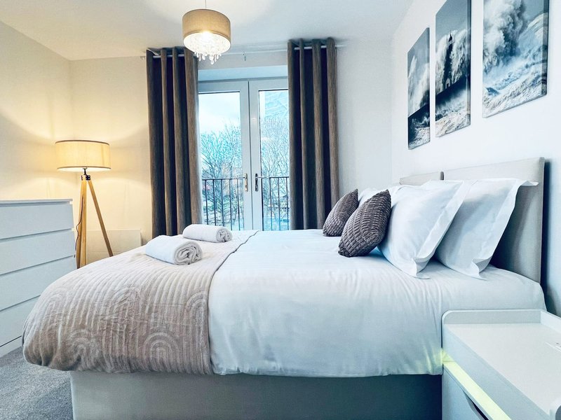 Modern bedroom with double bed, grey headboard, white bedding, dark curtains and balcony view
