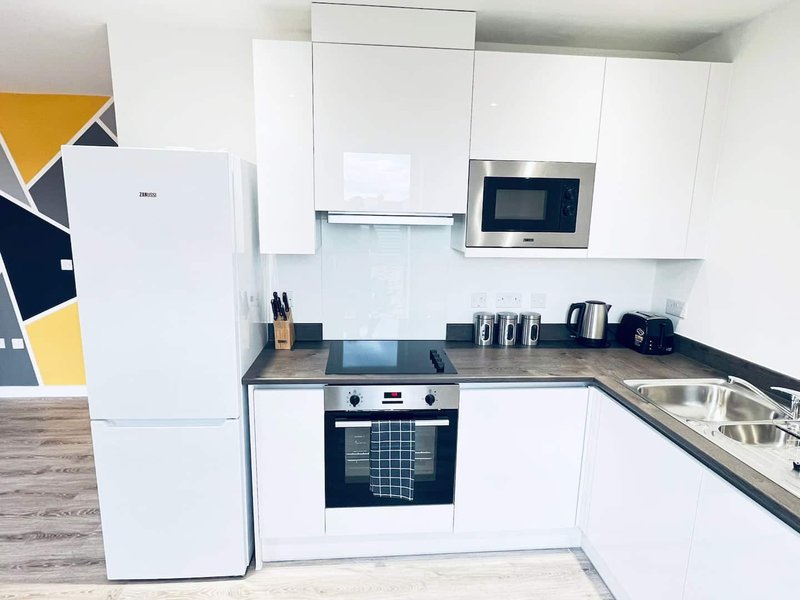 Modern white kitchen with built-in appliances, dark countertop, and geometric wall art