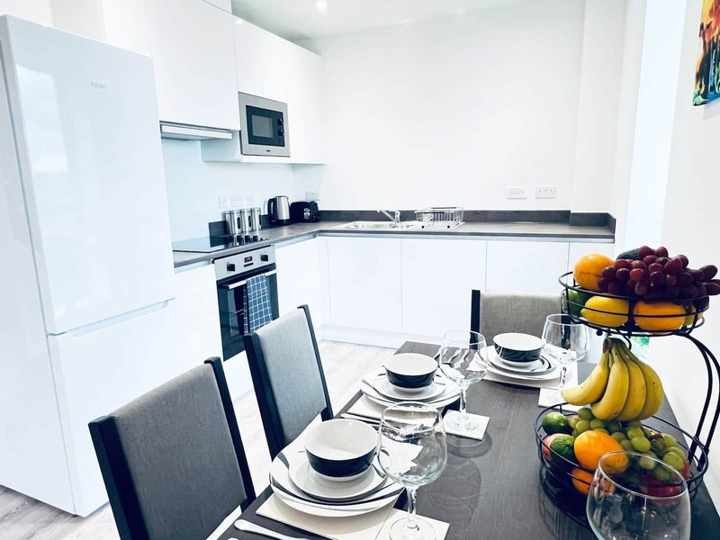 Modern kitchen and dining area with white cabinetry, dining table set for four, and fresh fruit display