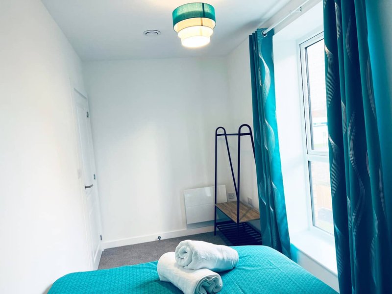 Compact bedroom with turquoise bedding, rolled towels, metal bed frame and teal curtains