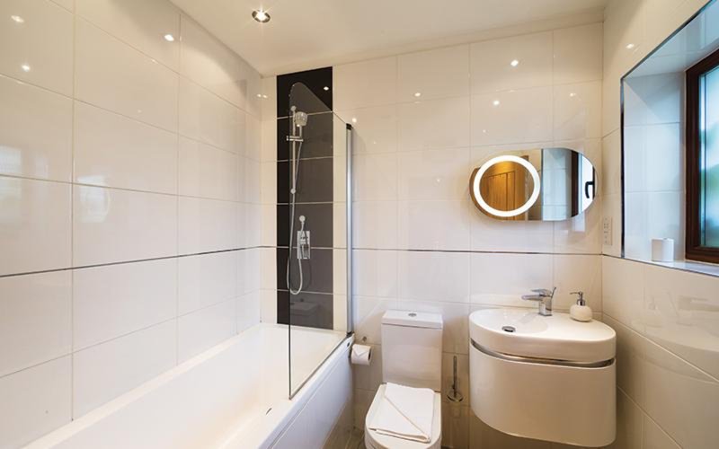 Modern bathroom with walk-in shower, toilet, sink and illuminated mirror