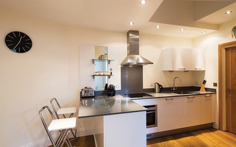 Modern open-plan kitchen with island, stainless steel range hood, dining area and wall clock