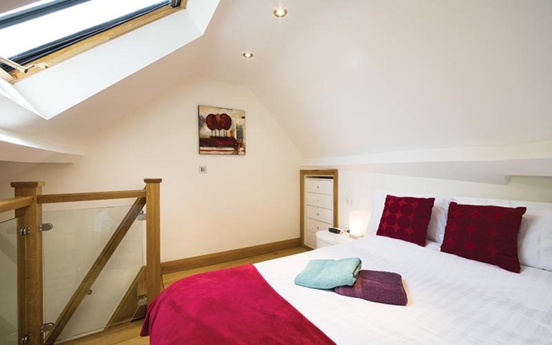 Bedroom with skylight, wooden beams, double bed with burgundy bedding and cushions