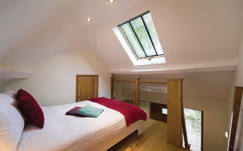 Bright attic bedroom with skylights, wooden bed frame, burgundy cushions and throws