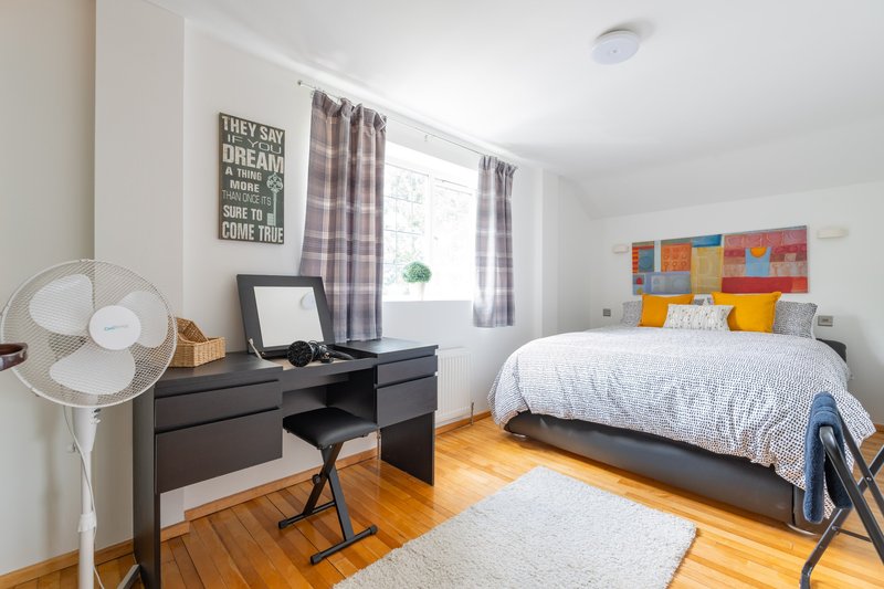 Bright bedroom with double bed, desk, wooden floor and plaid curtains