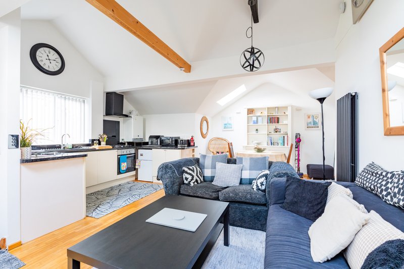 Open-plan living and kitchen area with blue sofa, wooden beams, and nautical decor