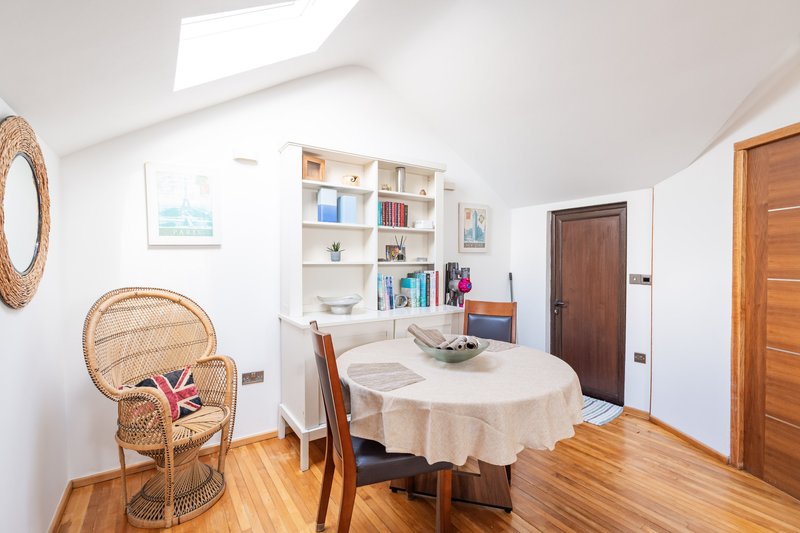Bright attic room with dining table, wicker chair, built-in shelving and wooden doors