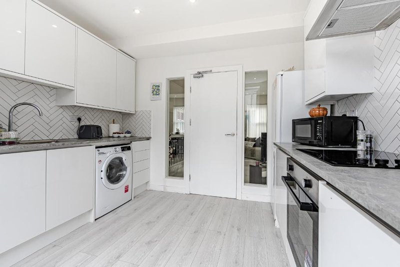 Modern white kitchen with herringbone tile backsplash, integrated appliances, and wooden flooring