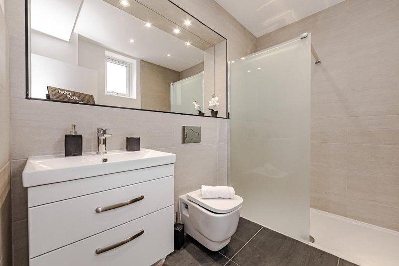 Modern bathroom with white vanity, large mirror, toilet, and walk-in shower enclosure