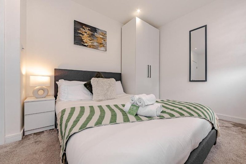 Modern bedroom with double bed, green striped throw, white wardrobe and bedside lighting