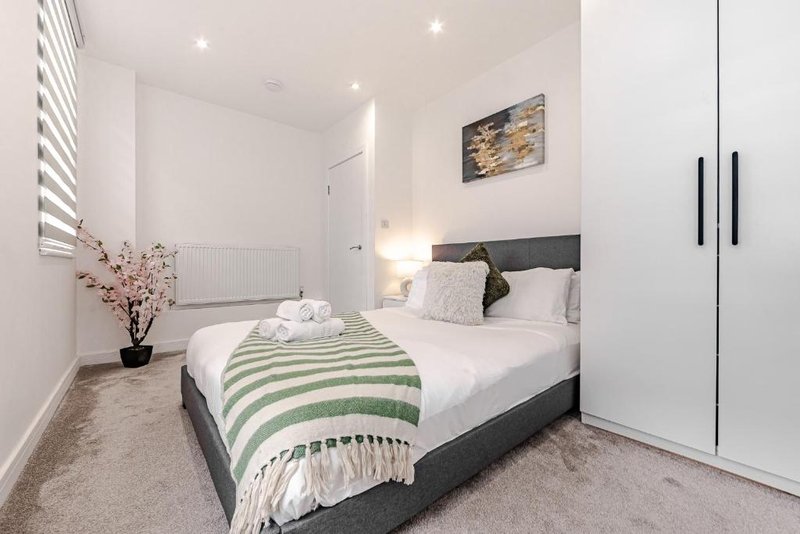 Modern bedroom with double bed, green striped bedding, white wardrobe and wall art