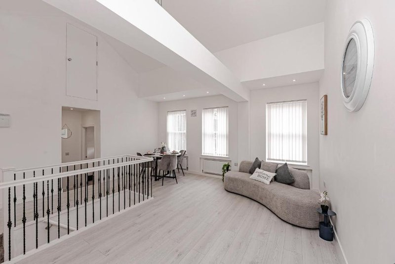 Bright open-plan living space with sofa, kitchen area, and metal stair railing