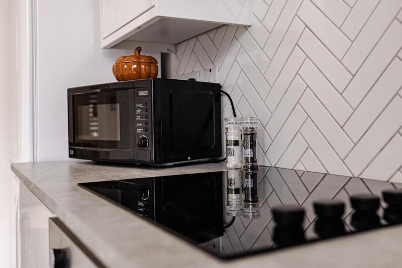 Modern kitchen counter with black microwave, toaster, decorative pumpkin and herringbone tile backsplash