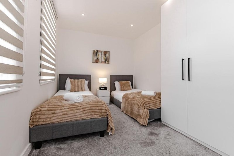 Twin bedroom with two single beds, striped blinds, white built-in wardrobe and bedside lighting
