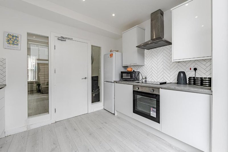 Modern white kitchen with built-in oven, hob, herringbone tile backsplash and light wooden flooring
