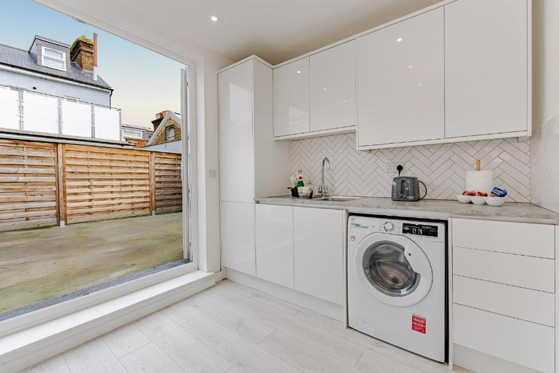 Modern white kitchen with washing machine, herringbone backsplash and garden view