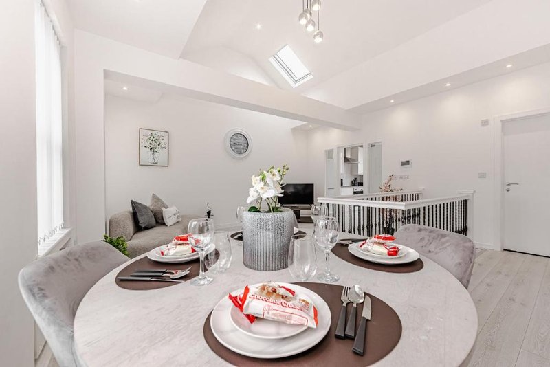 Modern open-plan dining and living space with round table, place settings, and kitchen area visible in background