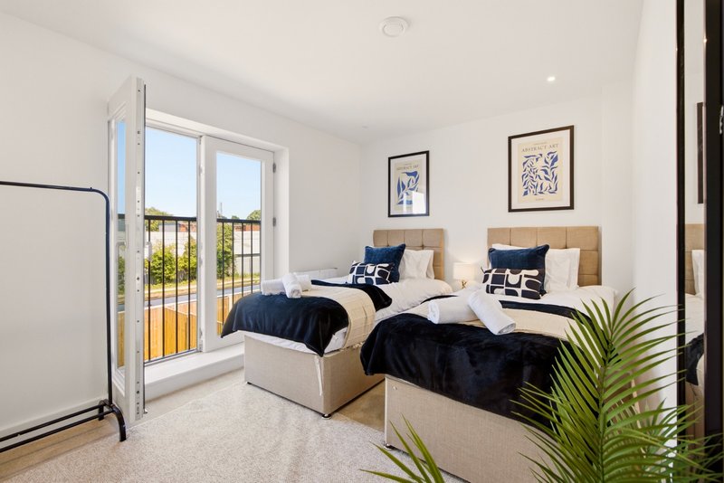 Bright twin bedroom with two single beds, blue bedding, framed artwork, and balcony access